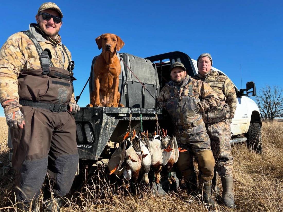 Three hunters and a fox red retriever at the truck with the morning's ducks