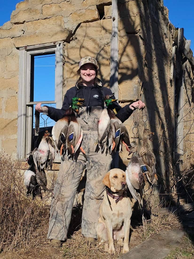 Hunter and a yellow lab holding up a strap of ducks in an old stone ruin