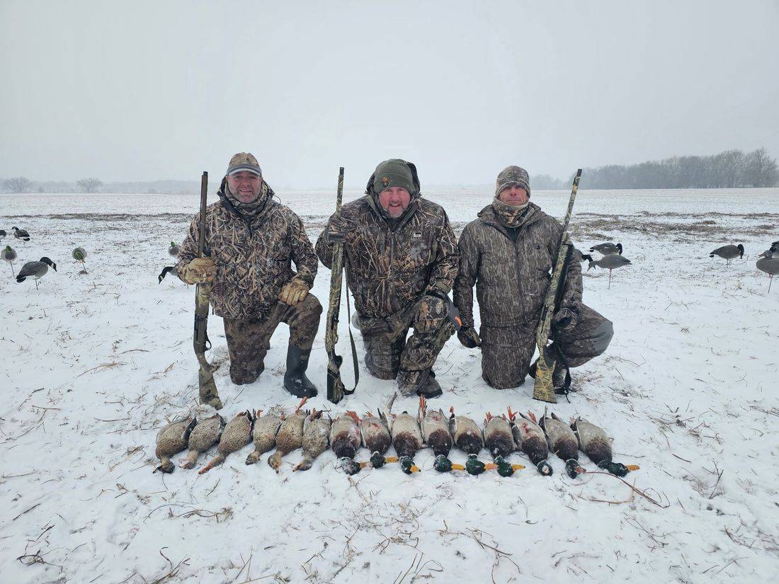 Three hunters kneeling behind a long line of ducks in the snow