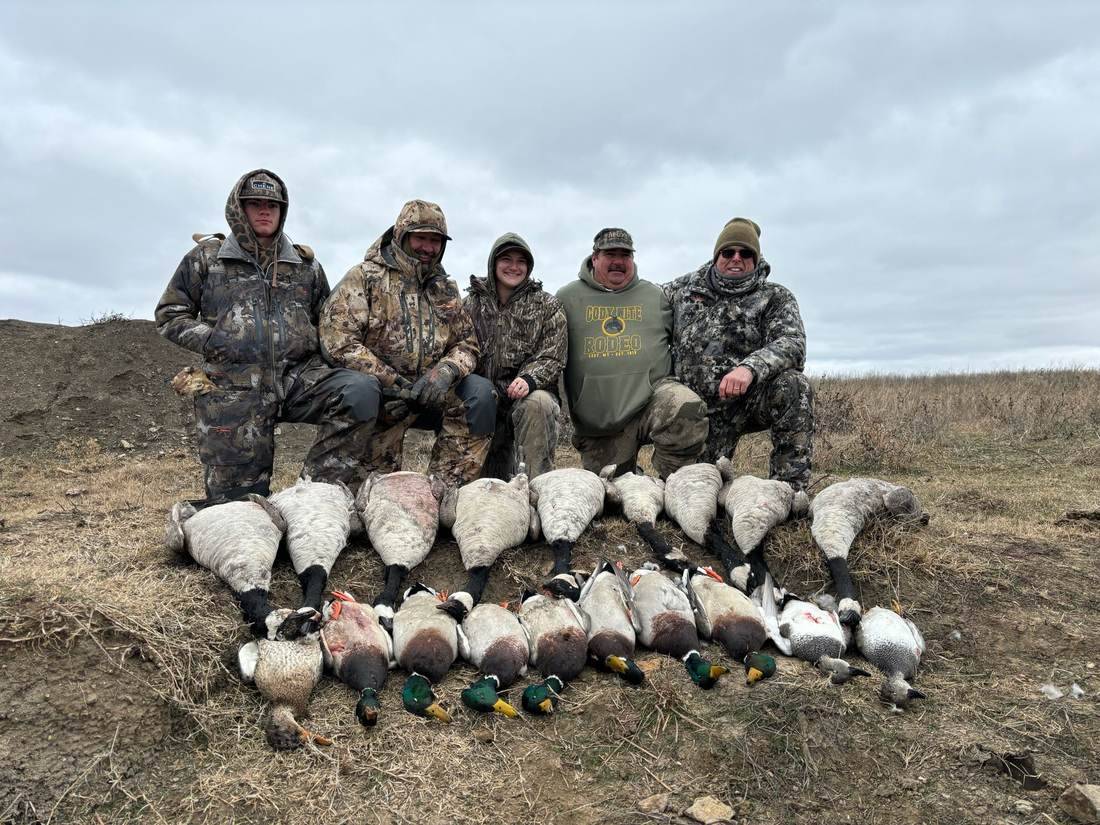 Group of hunters behind a spread of geese and ducks on the field edge