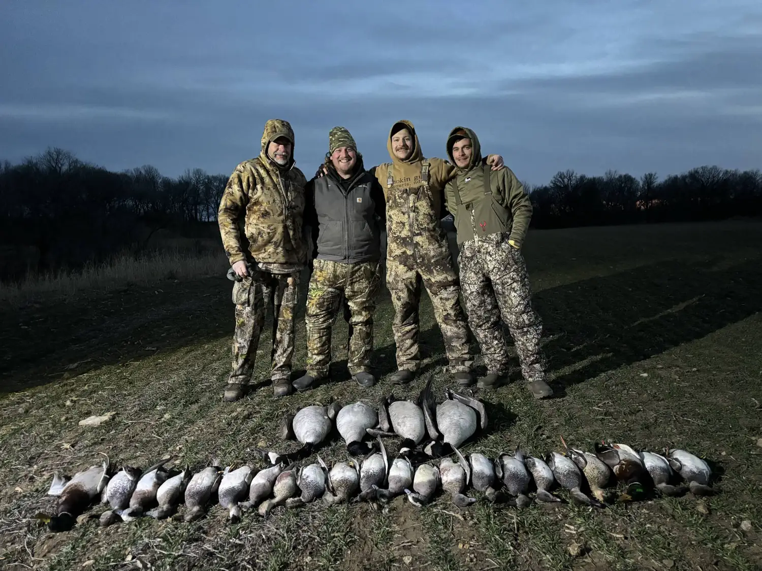 Hunting party standing behind a long field spread under a heavy morning sky